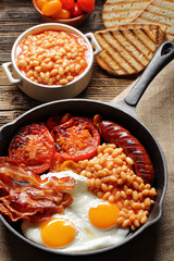 English Breakfast with sausages, grilled tomatoes, egg, bacon, beans and bread on frying pan.