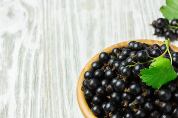 Ripe black currant in a wooden bowl on white shabby wooden table.  Selective focus, space for text.