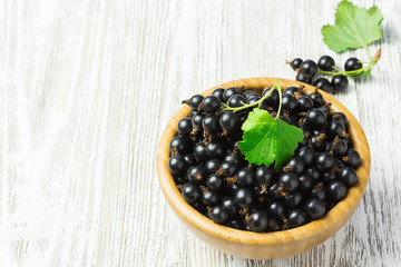 Ripe black currant in a wooden bowl on white shabby wooden table.  Selective focus, space for text.