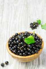 Black currant in a wooden bowl on white shabby wooden table. Summer snack, dessert.