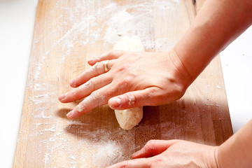 Fototapeta premium A woman in the kitchen is rolling a dough on a wooden table with hands.