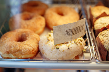 Coffee shop window with baked food, pastries. Closeup macro group of many round fresh organic doughnuts in basket with white paper