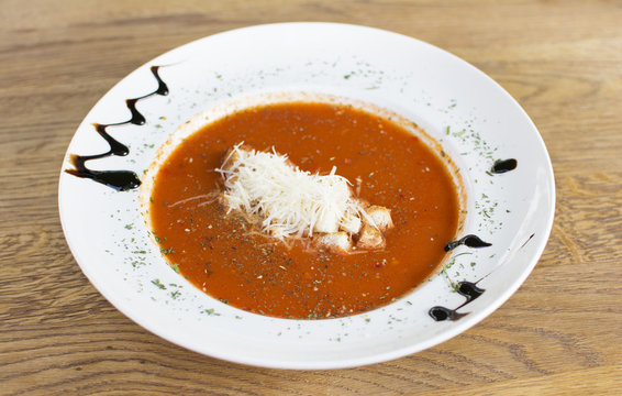 Tomato soup in a black bowl on wooden table. Top view.