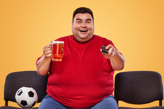 Soccer and sport fun - happy and fat man watching tv, taking beer and soccer ball on yellow background.