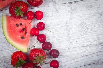 Watermelon, strawberries and cherries on wooden background.