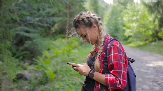 Happy girl standing in the forest and texting sms on smartphone