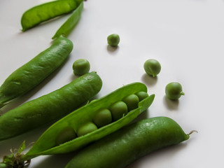 Abstract natural background - pea pods with peas close-up on a white background. Green young juicy pea pods lie in the bottom corner of the photo, and  small spherical seeds are scattered between them