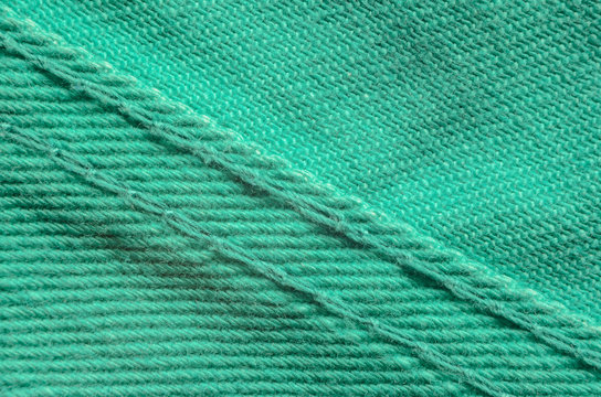 Green Denim Tissue Structure Textile Texture Close-up. Macro shot of the finishing seam on a green jeans product.