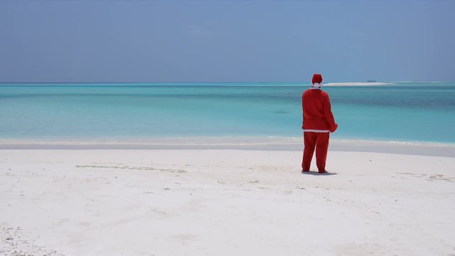 Man in Santa Claus costume on sandy tropical beach. Christmas and New Year celebration on Maldive island
