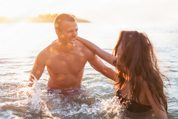 Couple having fun at the sea, sunset, splashing the water
