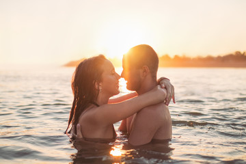Couple in water at sea, hugging, at sunset, golden hour - obrazy, fototapety, plakaty