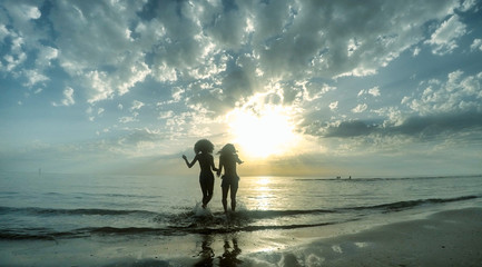 silhouette 2 girls friends on beach at sunset or dawn with cloudy sky background. concept of...