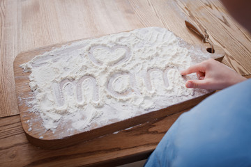 little son wrote by finger on a plaque with flour the word mom