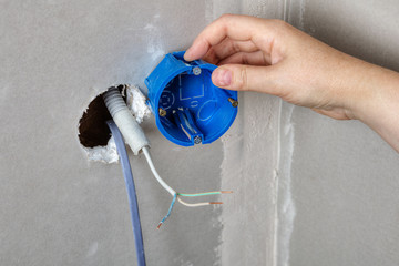 Install electrical box in the wall hole, hand close-up.