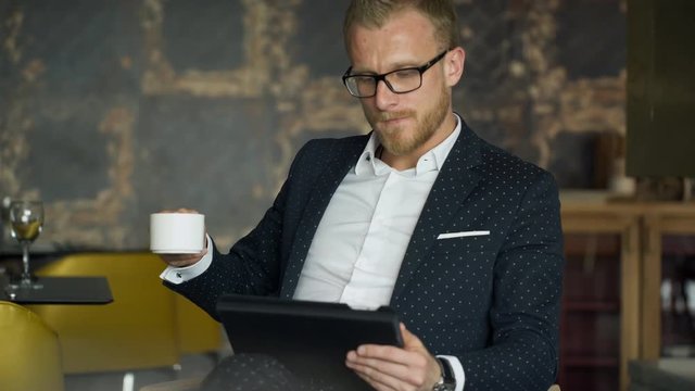 office worker sit in chair, looking documents on tablet in cafe. , drinking coffee, taking device, analyzes images, drawings, studies, notes required items next to table.