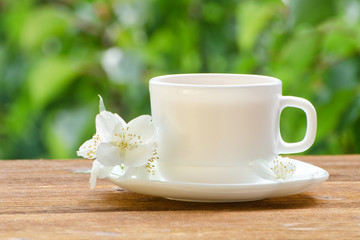 White mug of tea with jasmine on a background greenery, sunlight. Close-up