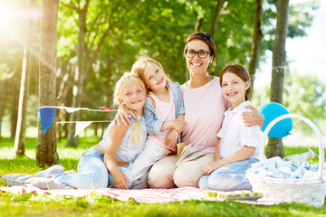 Kindergarten teacher and happy girls relaxing outdoors on summer day