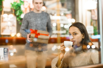 Young amorous man going to make surprise for his girlfriend while she having tea in cafe
