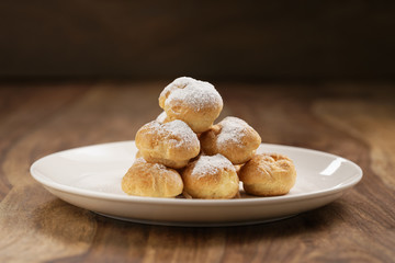 profiteroles covered with sugar powder on white plate on wooden table
