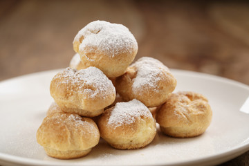 closeup shot of profiteroles covered with sugar powder on white plate on wooden table