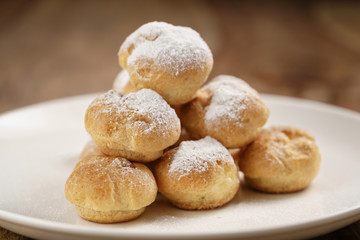 closeup shot of profiteroles covered with sugar powder on white plate on wooden table