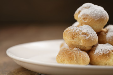 closeup shot of profiteroles covered with sugar powder on white plate on wooden table