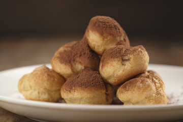 closeup shot of profiteroles covered with cocoa powder on white plate on wooden table