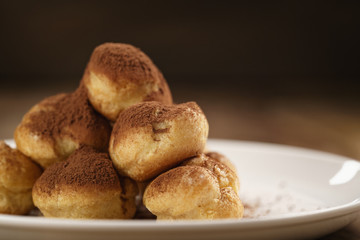 closeup shot of profiteroles covered with cocoa powder on white plate on wooden table