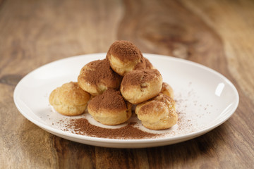 profiteroles covered with cocoa powder on white plate on wooden table