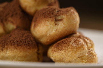 closeup shot of profiteroles covered with cocoa powder on white plate on wooden table