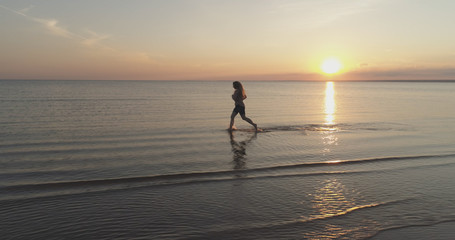 Fototapeta na wymiar Aerial shot over teen girl barefoot running in water on baltic sea beach in sunset time