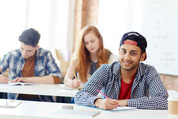 Fototapeta premium Clever teenage learner sitting by desk during exam and carrying out written task or writing essay