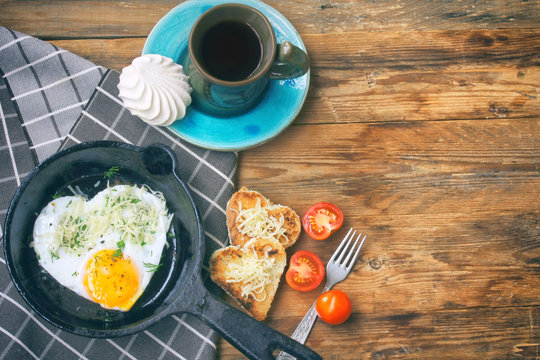 Fried eggs in a frying pan, toast with cheese heart shape, cup of coffee