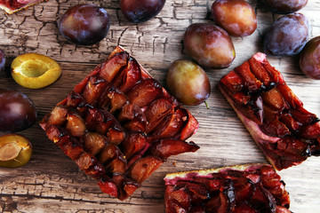 rustic plum cake on wooden background with plums around