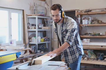 Young carpenter working with circular saw in shop