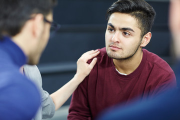Sad man listening to advice of colleague during group session