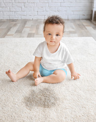 Little adorable girl sitting on carpet near wet spot