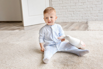 Cute baby boy sitting on carpet and playing with toy near wet spot