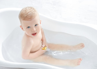 Little baby boy washing in bathtub at home