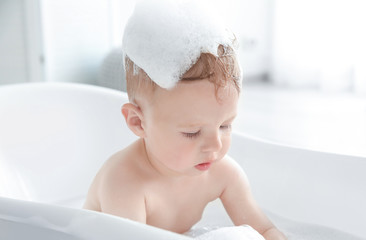 Little baby boy washing in bathtub at home