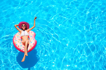 Fototapeta premium Beautiful young woman relaxing on inflatable donut in blue swimming pool