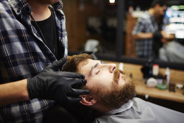 Beautician taking care of client face during massage procedure