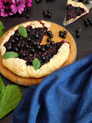 Galette with black currant and a piece of it on a dark background