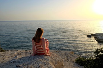 Tranquil seascape scene with girl which looking at the sun sitting on the rock at the beach. 
Kos island Greece.