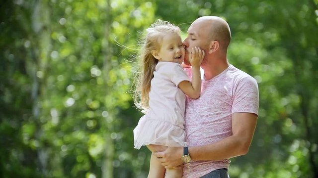 Happy father hugging and swinging his daughters in park, slow-motion