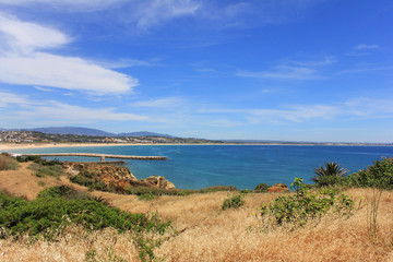 Fototapeta na wymiar Beautiful landscape overlooking Atlantic ocean coast in South Portugal. Summer nature panoramic scene: hills, water, beach and clear blue sky background. Photo of long distance outdoor sunny day view