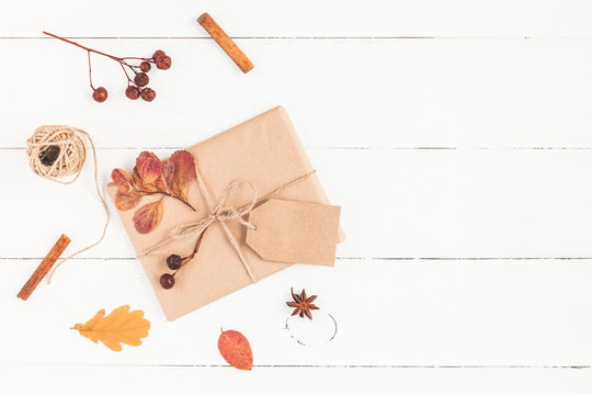 Autumn composition. Gift, autumn leaves, cinnamon sticks, anise star on wooden white background. Flat lay, top view, copy space
