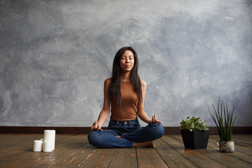 People, meditation and relaxation. Attractive brunette Korean girl wearing top and jeans sitting on...