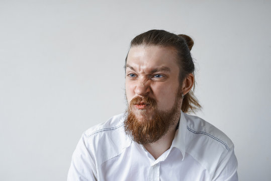 Picture of funny emotional young European office worker with facial hair grimacing, screwing nose, his look expressing dislike, discontent or dissatisfaction. Negative human reaction and attitude