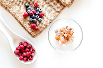 Making summer preserve. Raspberry, blueberry and sugar on white background top view copyspace